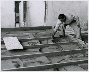 Nivola sculpting the sand in the forms referencing a small model, circa 1960